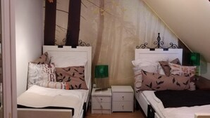 A bedroom with two beds, a nightstand, a lamp, and a wall with a tree branch decoration.