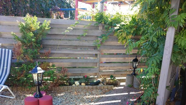 A garden with a wooden fence, a red planter, and a potted plant with flowers.