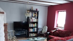 A living room with a bookshelf, a television, a red sofa, and a glass coffee table.