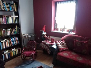 A cozy living room with a red sofa, a rocking chair, and a bookshelf filled with books. - Ferienhaus Badetz (Hohenlepte)