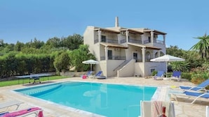 Um edifício de dois andares com piscina, cadeiras de descanso e guarda-sóis.