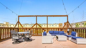 Una terraza exterior con una pérgola de madera, muebles de mimbre y una mesa de comedor con sillas.
