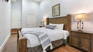 Un dormitorio con cama de madera, paredes blancas, mesita de noche de madera y un ventilador de techo.