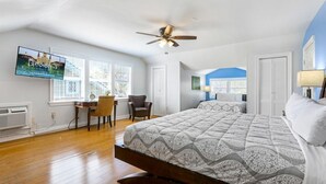 A spacious bedroom with a large bed, a desk, a chair, and a television displaying a cityscape.