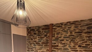 Un dormitorio con pared de piedra, suelo de madera, una cama con ropa de cama blanca y dos lámparas de noche.