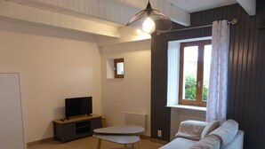 Una sala de estar con un sofá, un televisor sobre un mueble bajo, una mesita y una ventana con cortinas.