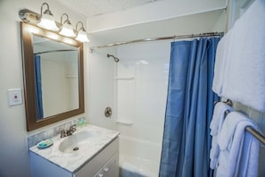 A bathroom with a large mirror, a sink, a shower, and a towel rack. - Island Manor Resort by VRHost (Block Island)