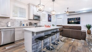 Una cocina moderna con armarios blancos, una isla central con taburetes de bar, un sofá marrón y un ventilador de techo.