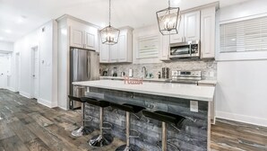 Una cocina moderna con armarios blancos, un refrigerador de acero inoxidable, horno empotrado, microondas e una isla grande con taburetes de bar.