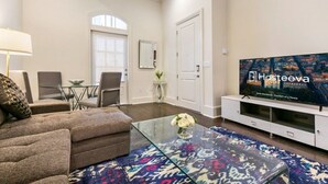 Un salon comprenant un canapé, une table basse en verre, un téléviseur et un coin repas avec des chaises et une table.