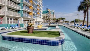 A hotel pool area with blue-tiled edges, lounge chairs, and a palm tree. - Floor to Ceiling Windows at Atlantica Resort 🍹Oceanfront 🍹 (Myrtle Beach)