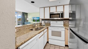 A modern kitchen with a granite countertop, stainless steel appliances, and white cabinetry. - Floor to Ceiling Windows at Atlantica Resort 🍹Oceanfront 🍹 (Myrtle Beach)