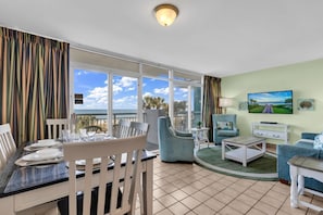 A room with a dining table set for four, a sofa, a TV, and a balcony with a view. - Floor to Ceiling Windows at Atlantica Resort 🍹Oceanfront 🍹 (Myrtle Beach)
