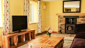 A living room with a television on a wooden stand, a coffee table, a sofa, a fireplace, and a mirror on the wall. - Sunnyside (Leominster)