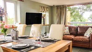 A dining area with a wooden table set for four, a television above the table, and a leather sofa in the background. - Sunnyside (Leominster)