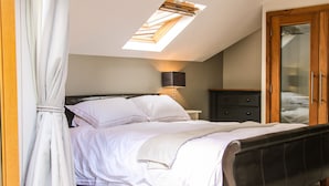 A bedroom with a bed, a nightstand, a lamp, a wardrobe, and a skylight. - Sunnyside (Leominster)