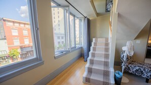 Une pièce dotée d’une grande fenêtre, d’un escalier recouvert d’une moquette à motifs, d’un ventilateur blanc et d’un canapé à motifs.