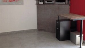 Un saló modern amb televisió plana, un moble gris, un moble petit negre, una taula de fusta i una paret vermella decorativa.
