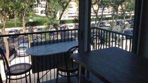 Un balcó amb taula i cadires, amb vista a un carrer amb cotxes aparcats i edificis.