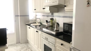 Uma cozinha com armários brancos, bancada preta, pia, fogão e micro-ondas.