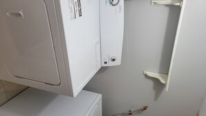 Ein Waschraum mit gestapelten Waschmaschinen und Trocknern, einer an der Wand montierten Steuerung und einer sichtbaren Wasserleitung.