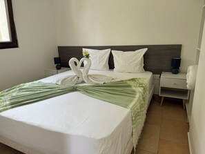 A neatly made bed with a green and white striped blanket, two white pillows, and a decorative swan towel arrangement.