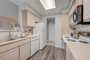 A modern kitchen with light wood cabinets, a white refrigerator, a dishwasher, a stove, and a skylight. - Central Houston- Urban Living (Houston)