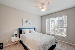 A bedroom with a bed, nightstand, ceiling fan, window, and artwork on the wall. - Central Houston- Urban Living (Houston)