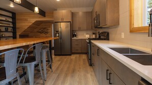 A modern kitchen with wooden cabinets, a stainless steel refrigerator, and a bar area with bar stools. - Great Family Getaway on the East side of Traverse City (Traverse City)