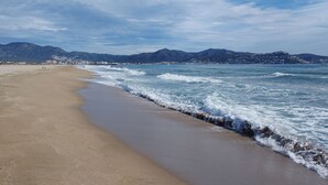 Una playa con arena, olas, montañas al fondo y un cielo despejado.