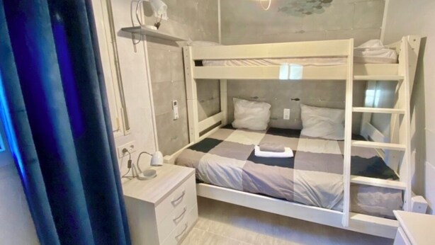 Habitación con literas, un escritorio, un espejo y una lámpara colgante.