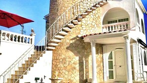 Una torre de piedra con escalera de caracol, un edificio blanco con balcón, y un paraguas rojo.