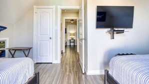 A hotel room with two beds, a flat-screen TV mounted on the wall, and a hallway leading to a bathroom. - Modern A-Frame | 3BR/2BA | Pet-Friendly | Steps to Beach | Huge Deck (Freeport)