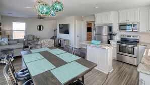 A modern kitchen with white cabinets, stainless steel appliances, and a dining area with a wooden table and chairs. - Modern A-Frame | 3BR/2BA | Pet-Friendly | Steps to Beach | Huge Deck (Freeport)