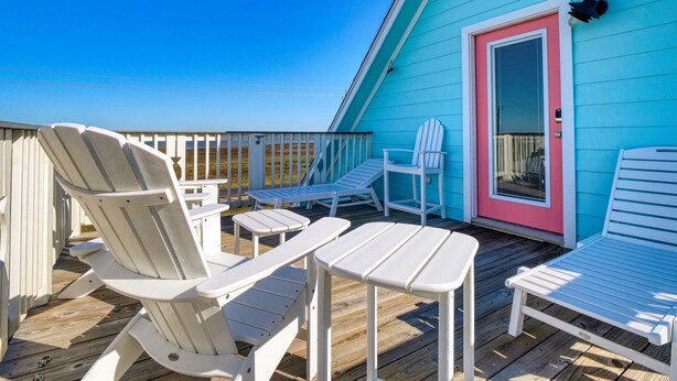A deck with white Adirondack chairs and tables, a pink door, and a blue building. - Modern A-Frame | 3BR/2BA | Pet-Friendly | Steps to Beach | Huge Deck (Freeport)
