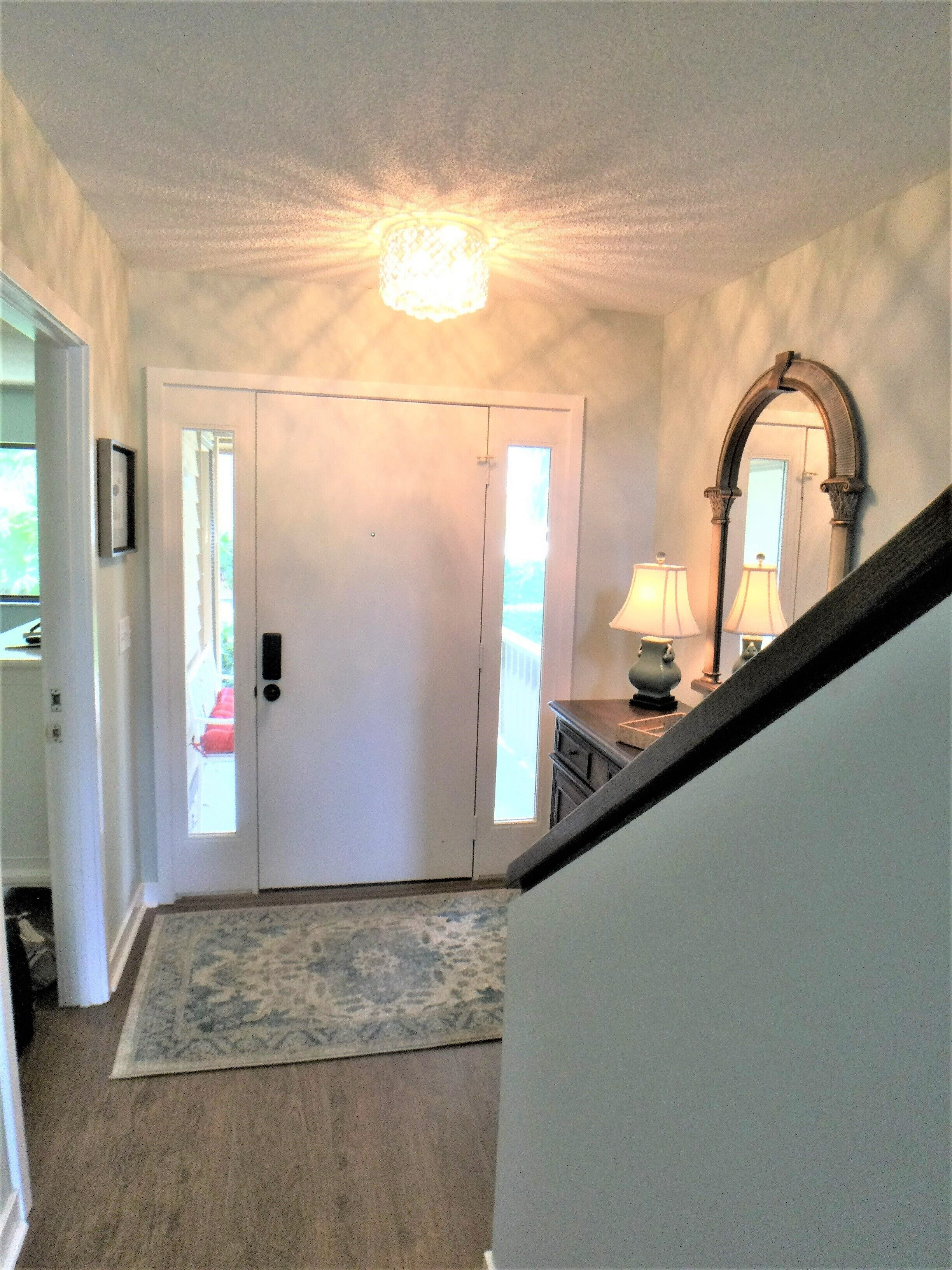 A hallway with a white door, a rug, a lamp, and a mirror on the wall.
