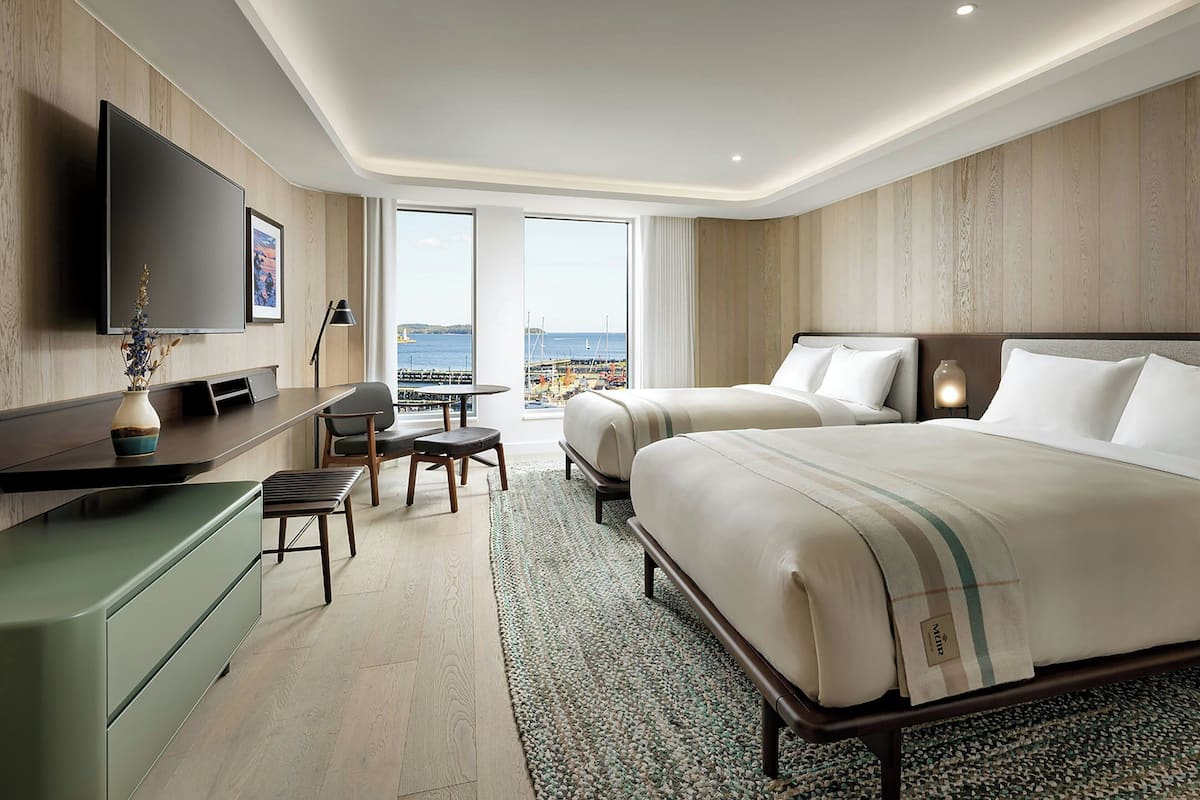 A hotel room with a large bed, a desk, a chair, and a TV mounted on the wall.