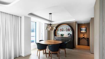 Un comedor moderno con una mesa redonda de madera y cuatro sillas, una lámpara colgante y una zona de bar con botellas y un cuadro.