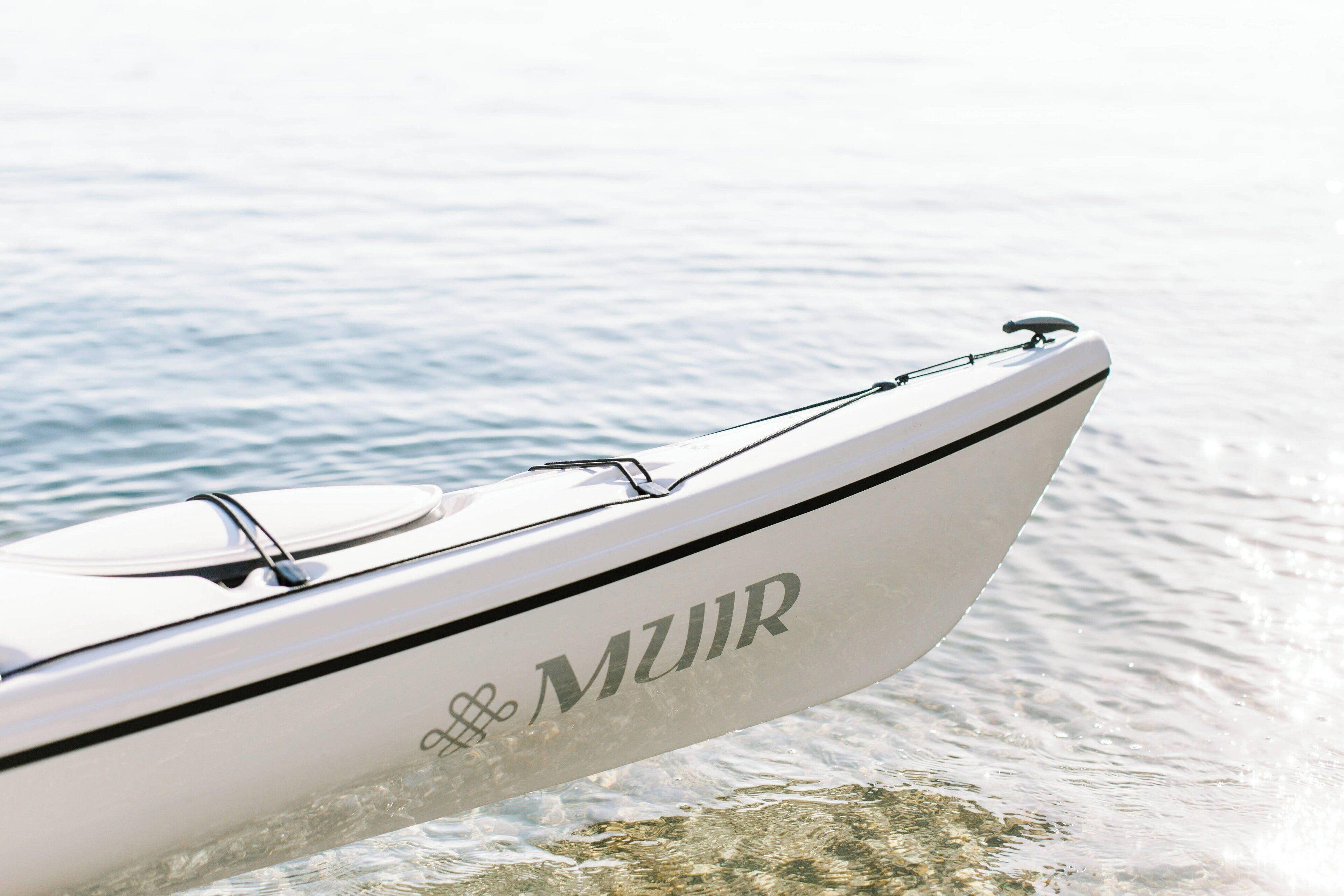 A boat with the name "MUIR" on its side, docked at a calm body of water.