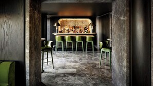 Una zona de bar con mostrador de mármol, taburetes verdes y suelo de piedra.