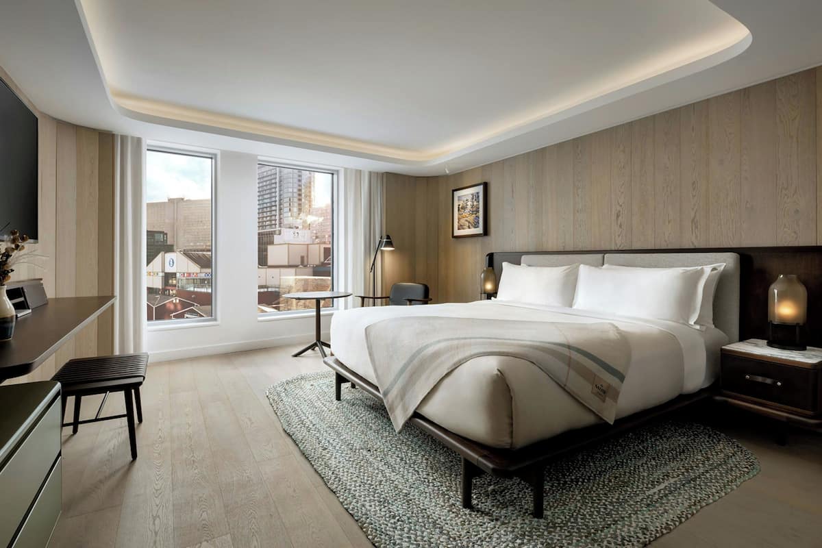 A modern hotel room with a large bed, bedside tables, a desk, and a view of the city.