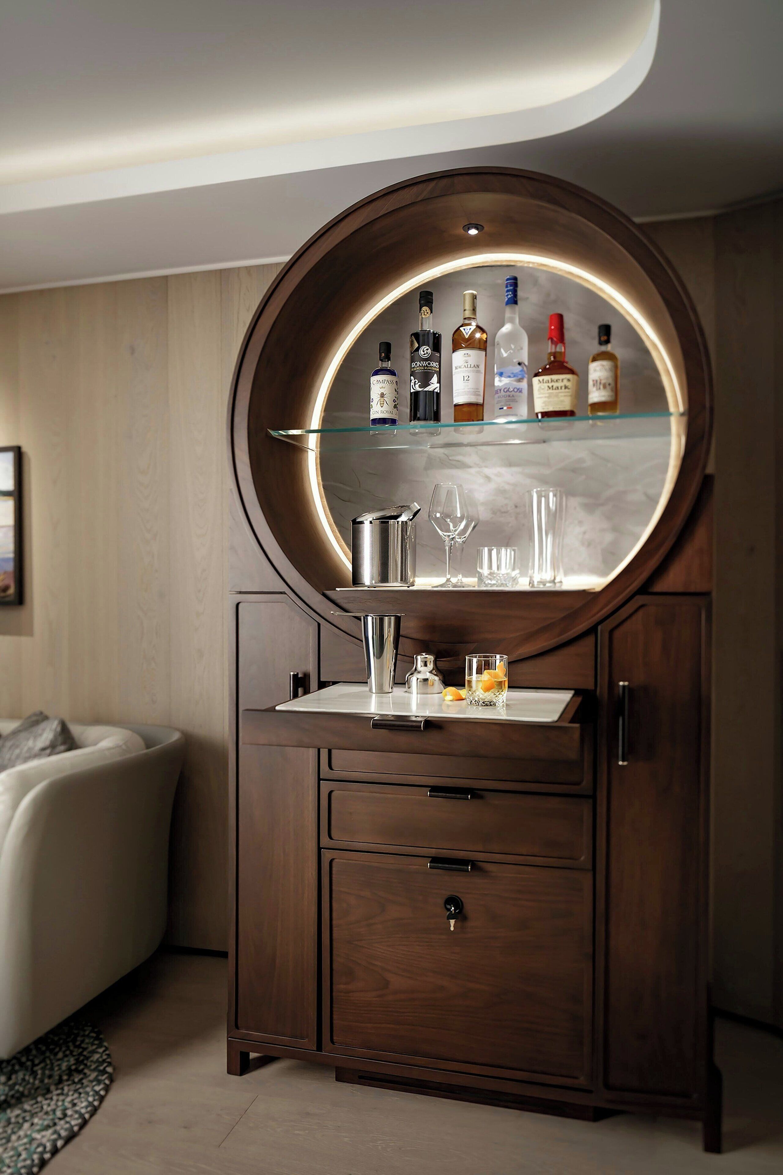 A wooden cabinet with a round mirror, shelves with bottles, and glasses.
