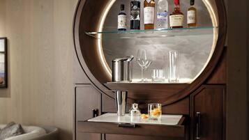 A wooden cabinet with a round mirror, shelves with bottles, and glasses.