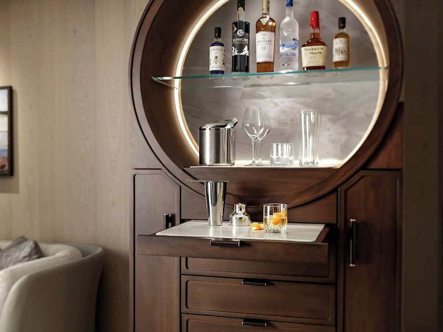 A wooden cabinet with a round mirror, shelves with bottles, and glasses.