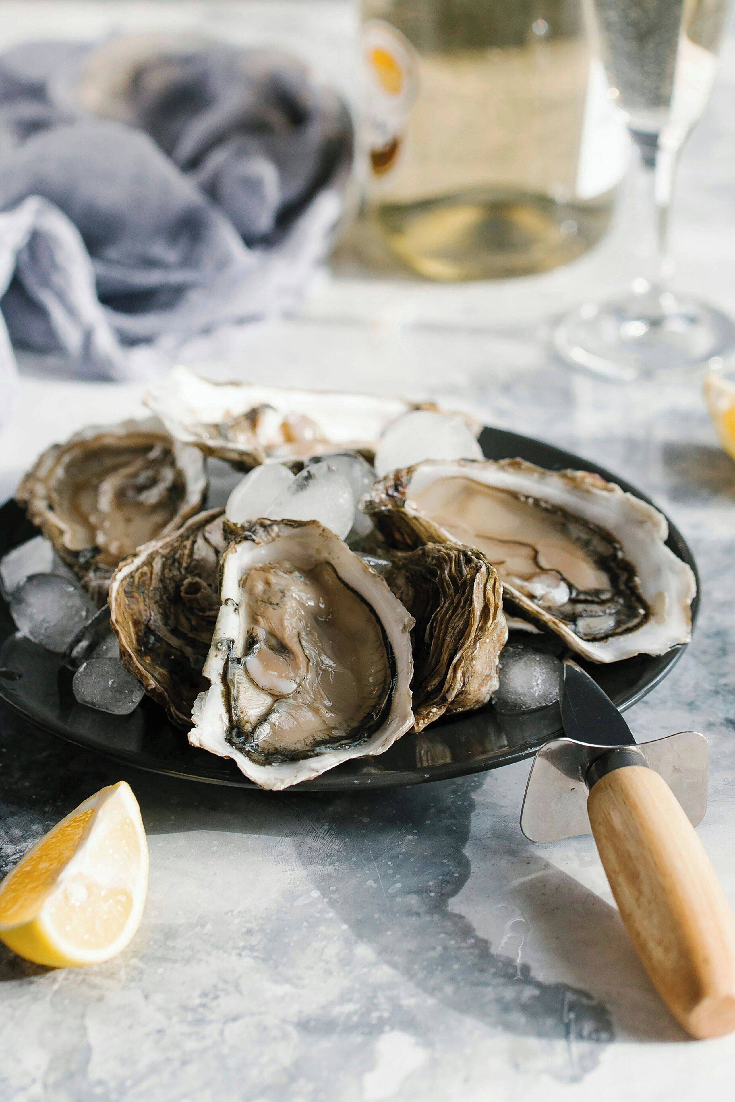 A plate of oysters on ice with a knife and a lemon wedge.