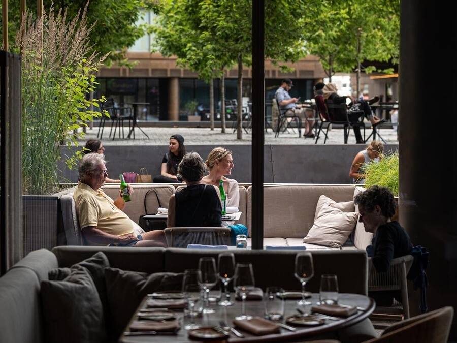 An outdoor seating area with tables and chairs, overlooking a street with people and buildings.