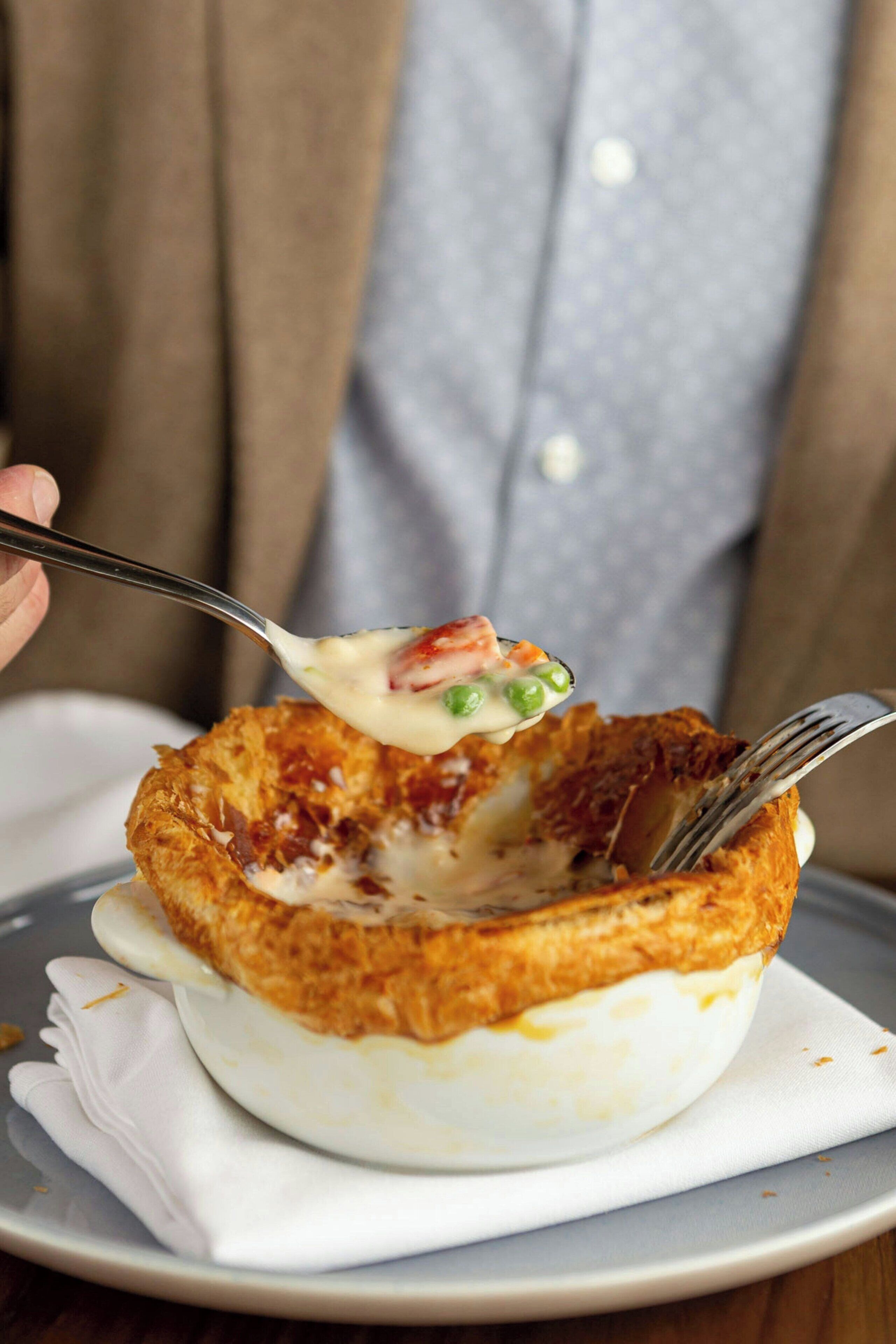 Una persona che tiene un cucchiaio con una zuppa cremosa con piselli e un pezzo di carne.