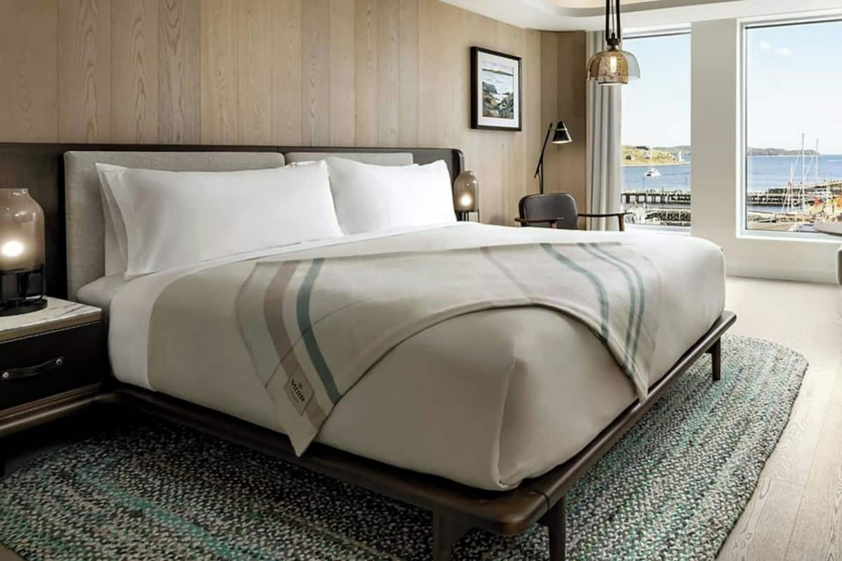 A hotel room with a large bed, a view of the sea, and a wooden wall.