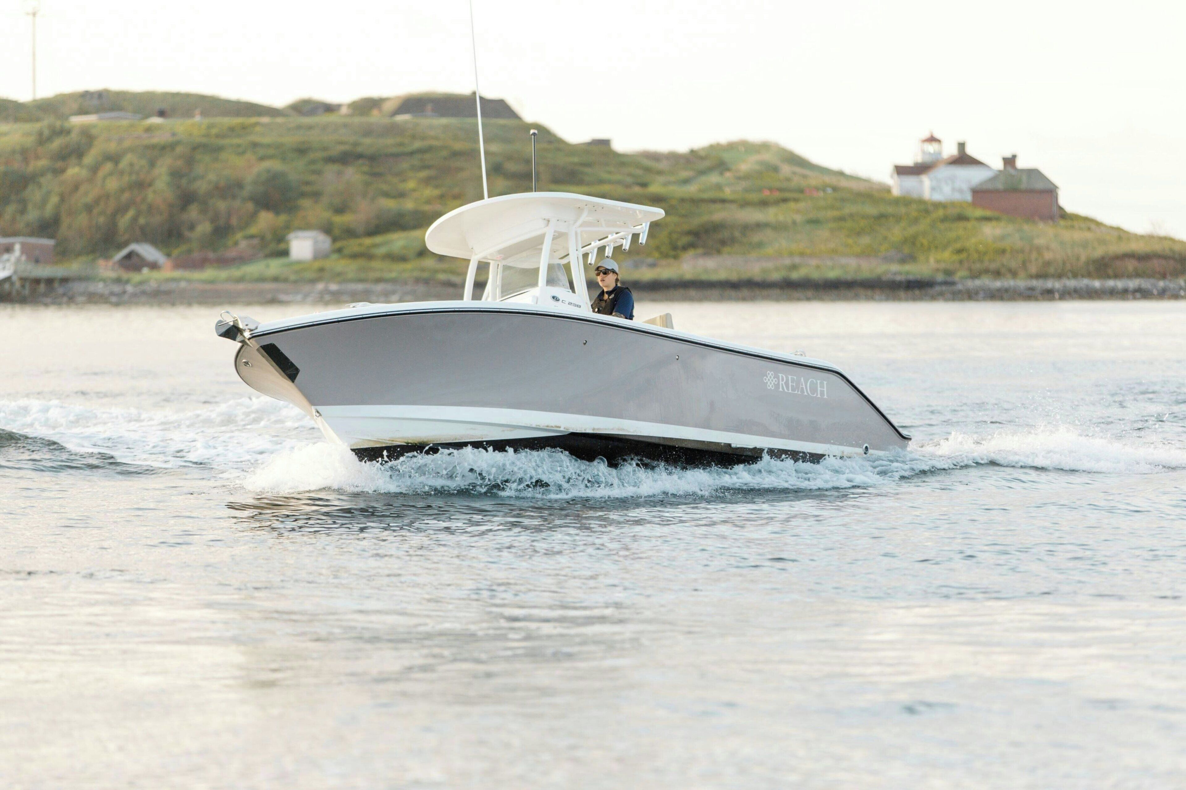 A sleek, modern boat with a covered deck, moving through calm waters with a hilly landscape in the background.