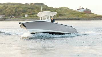 A sleek, modern boat with a covered deck, moving through calm waters with a hilly landscape in the background.